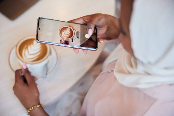 Independent café owner taking a photo of latte art on a smartphone